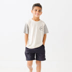 Child wearing a white t-shirt with checkered sleeves and black shorts on a white background