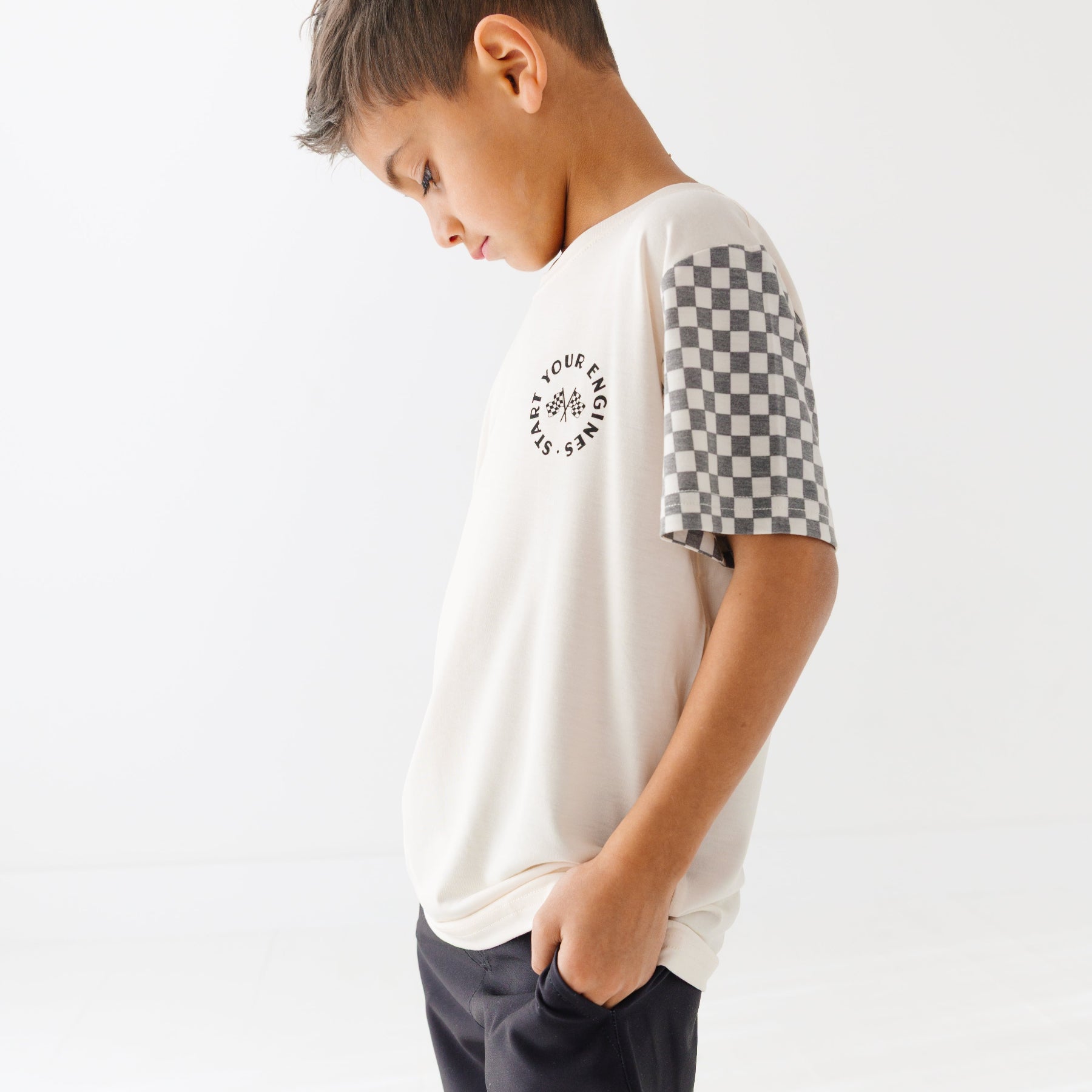 Child wearing a white t-shirt with checkered sleeves and black shorts on a white background