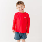 Child wearing a red rash guard and dark blue shorts on a white background