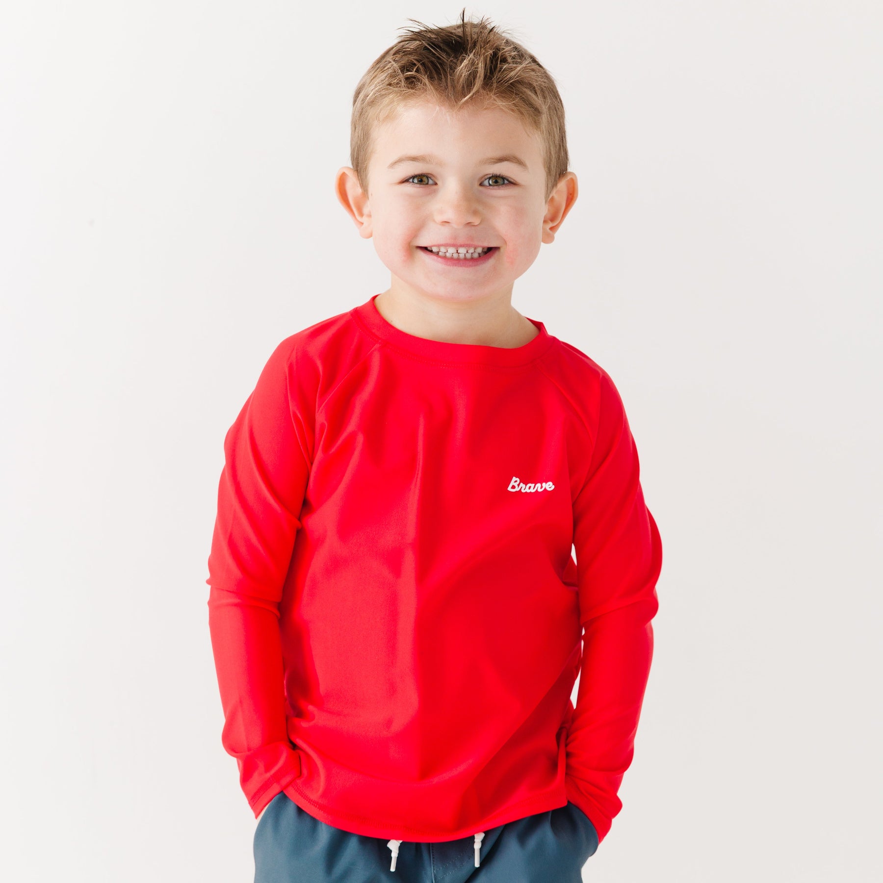 Child wearing a red rash guard with a logo on a white background