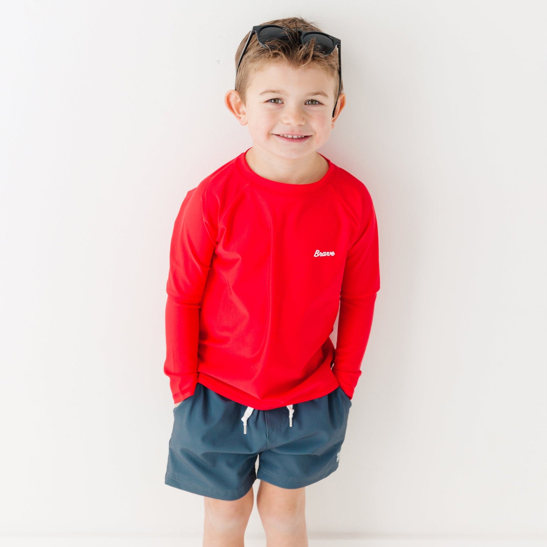 Child wearing a red rash guard and dark blue shorts on a white background