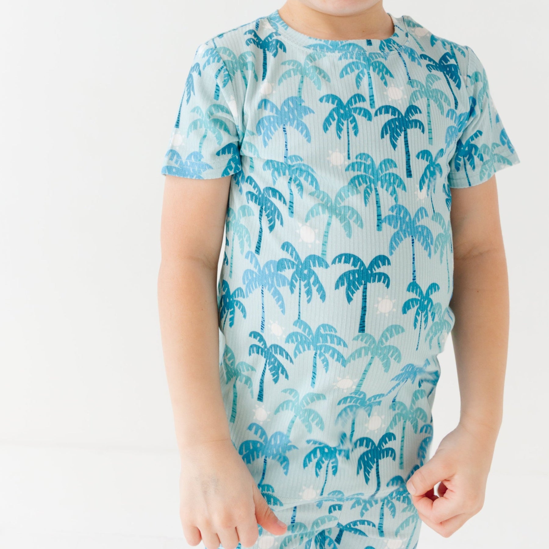 Child wearing a blue palm tree patterned pajama on a white background