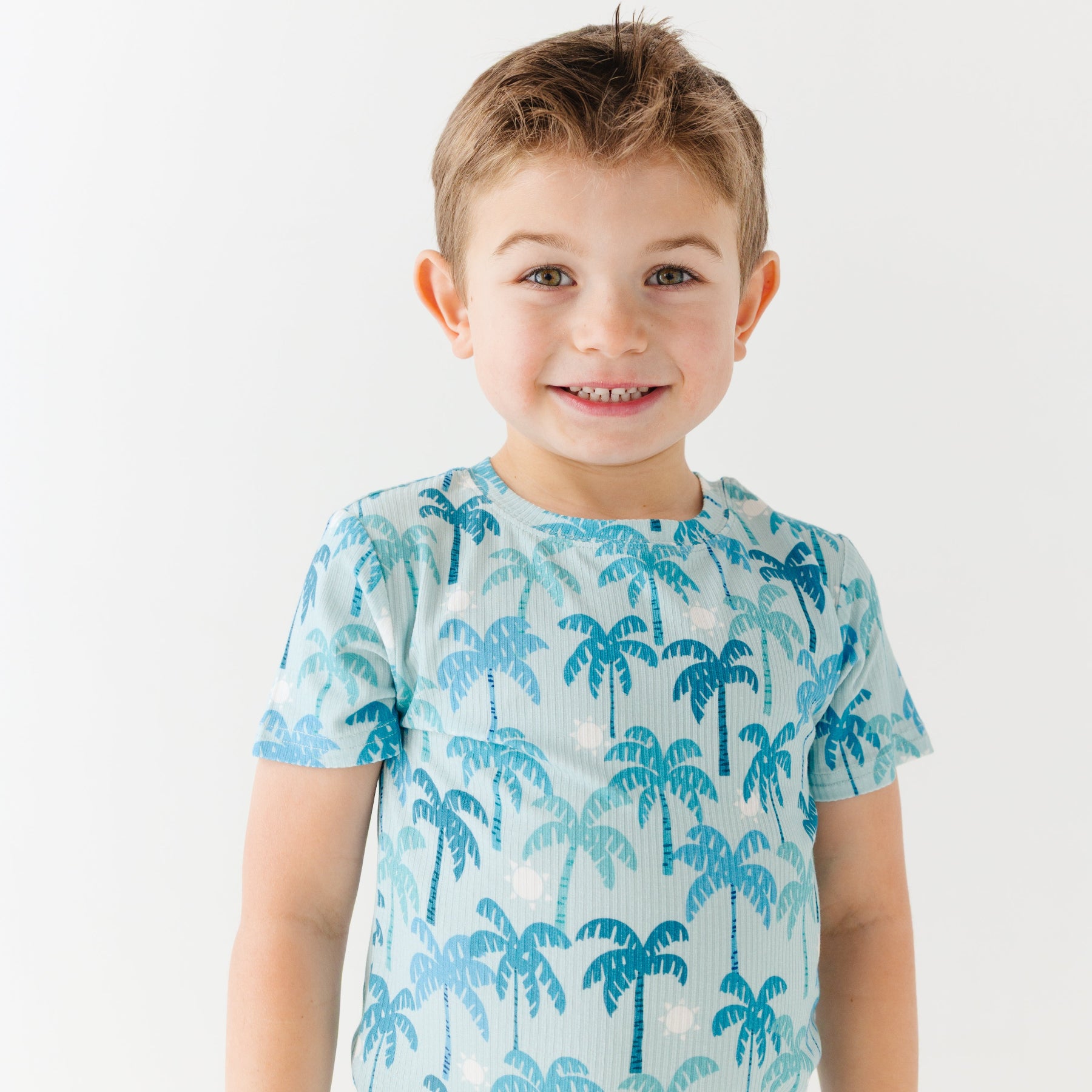 Child wearing a blue palm tree patterned pajama shirt on a white background