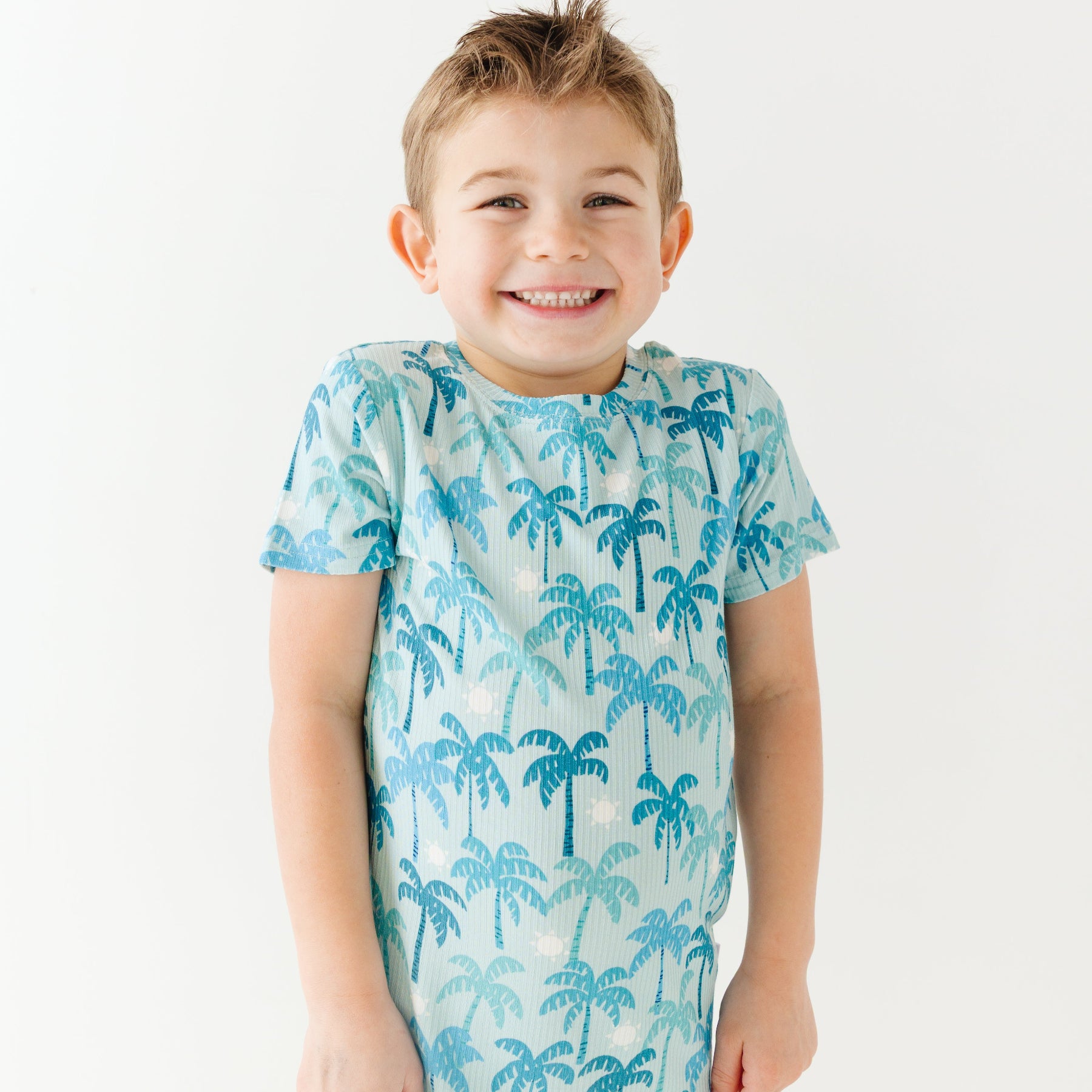 Child wearing a blue palm tree patterned pajama shirt on a white background