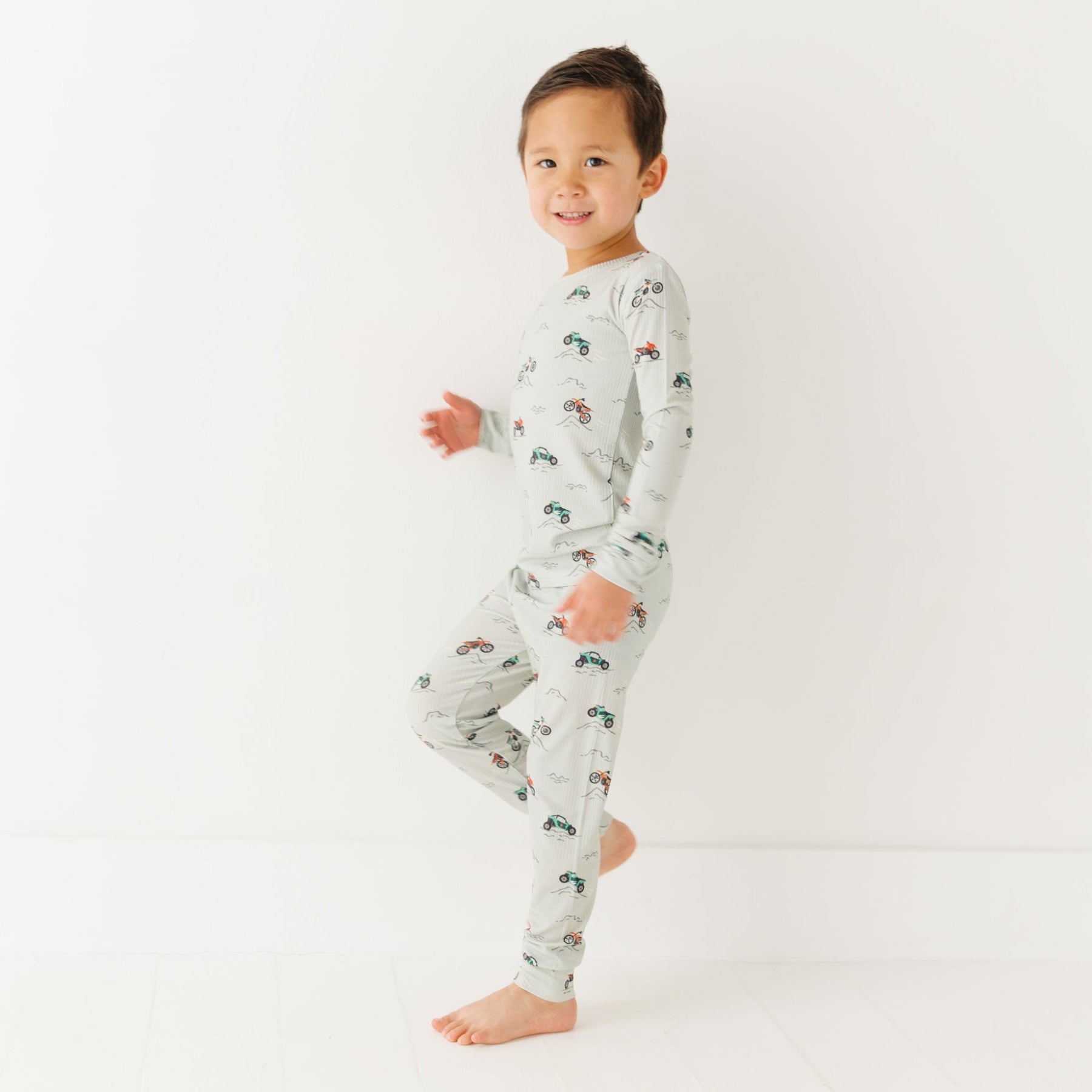 Child wearing a long sleeve pajama set with vehicle patterns on a white background