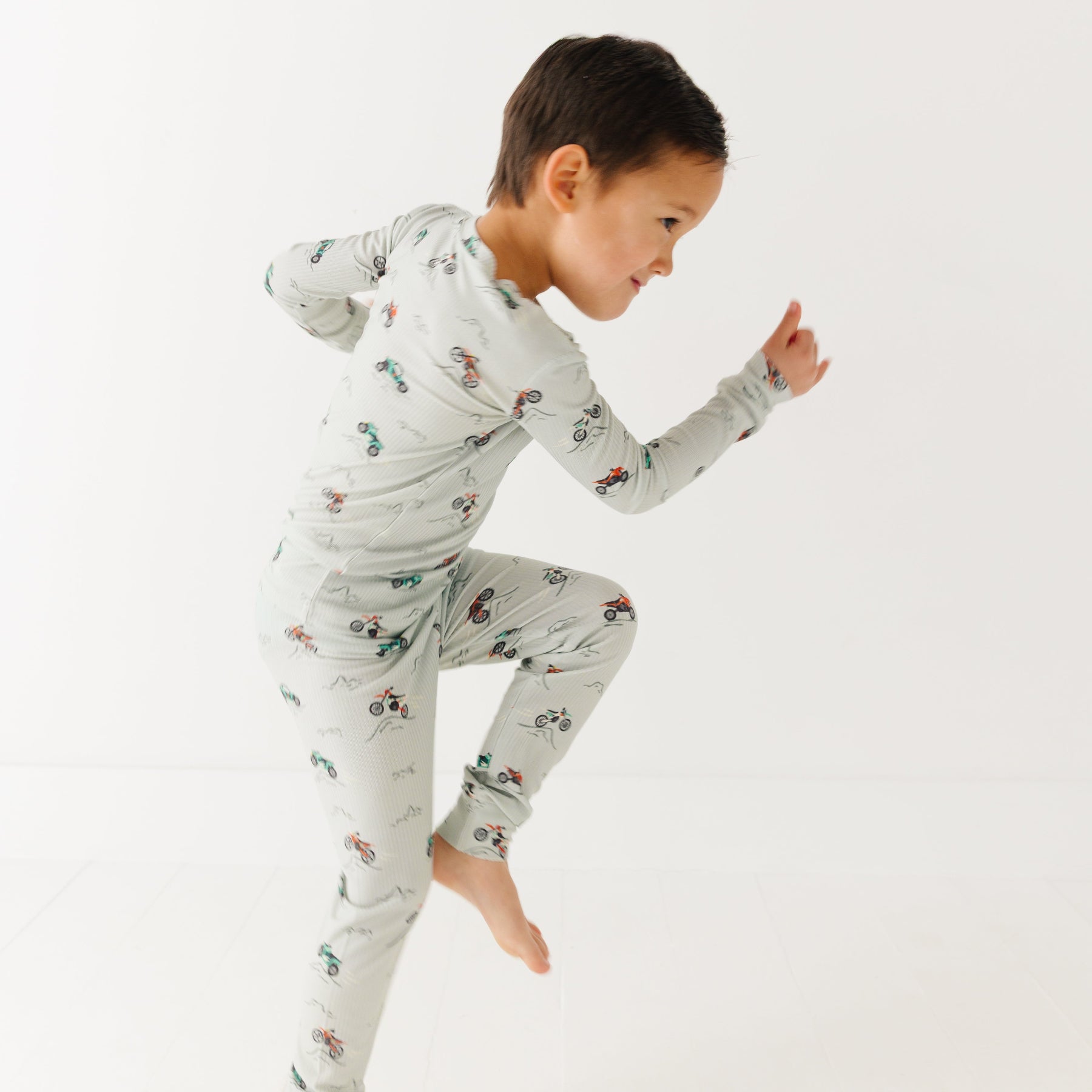 Child wearing a long sleeve pajama set with vehicle patterns on a white background