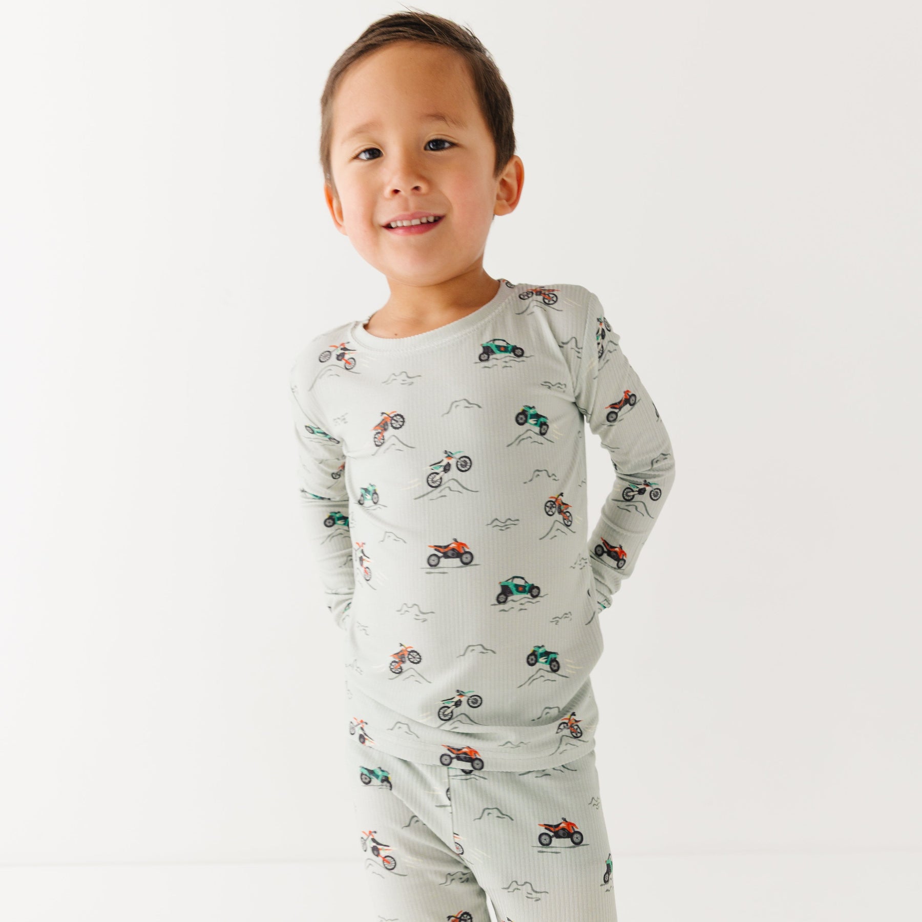 Child wearing a long sleeve pajama set with vehicle patterns on a white background