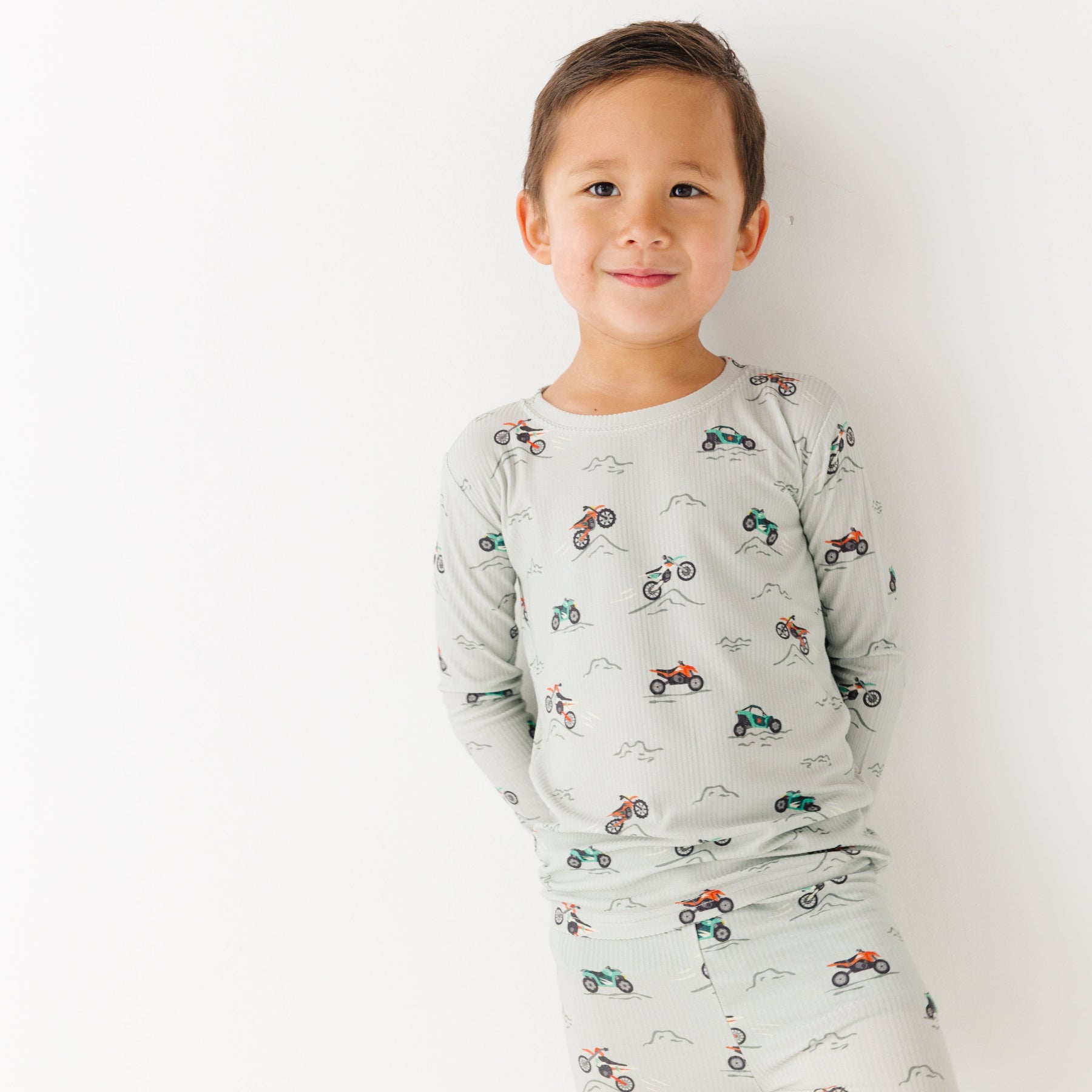 Child wearing a long sleeve pajama set with vehicle patterns on a white background