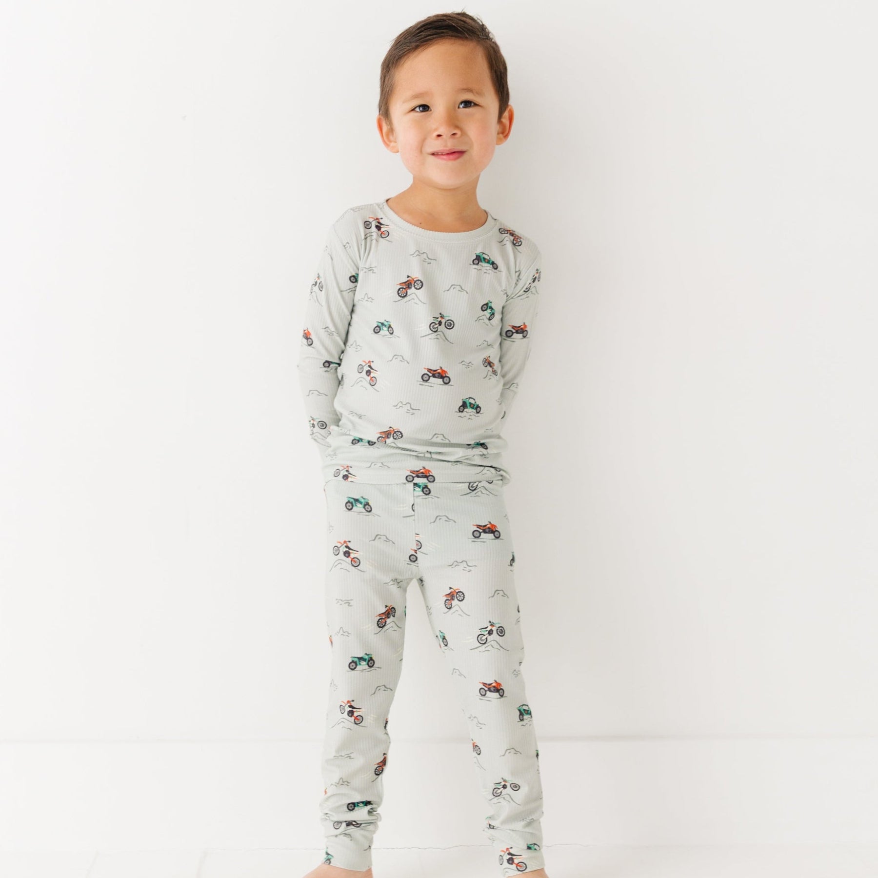 Child wearing a long sleeve pajama set with vehicle patterns on a white background
