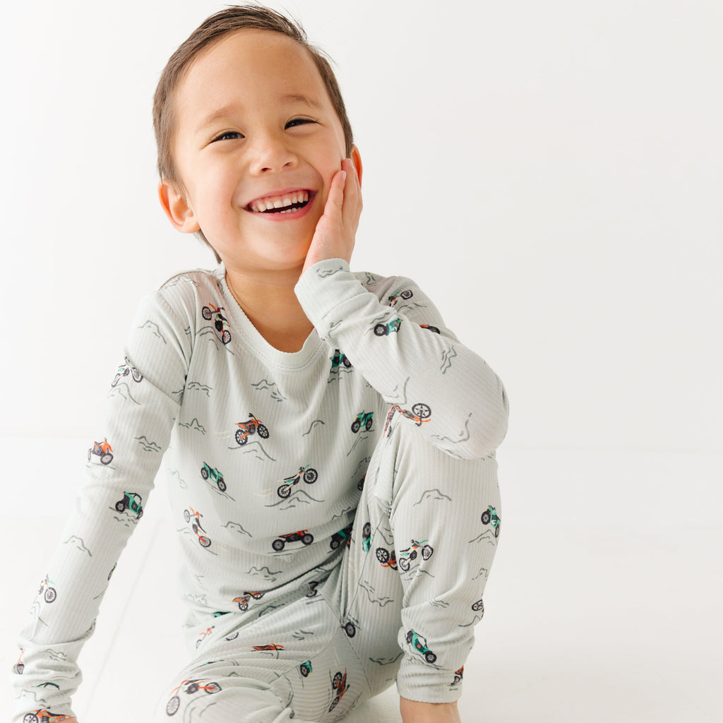 Child wearing a long sleeve pajama set with vehicle patterns on a white background