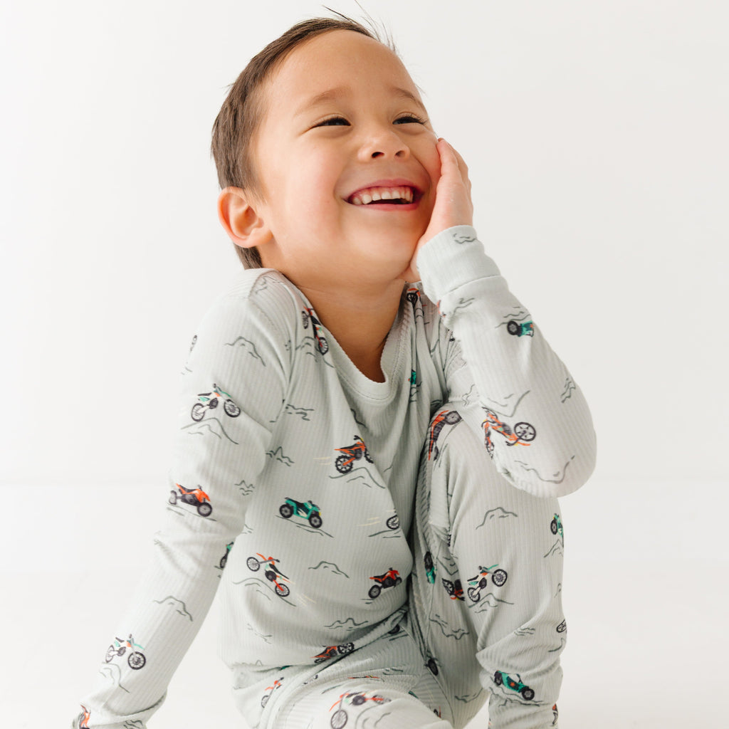 Child wearing a long sleeve pajama set with vehicle patterns on a white background