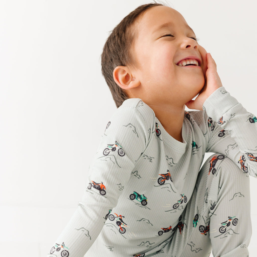 Child wearing a long sleeve pajama set with vehicle patterns on a white background