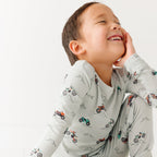 Child wearing a long sleeve pajama set with vehicle patterns on a white background