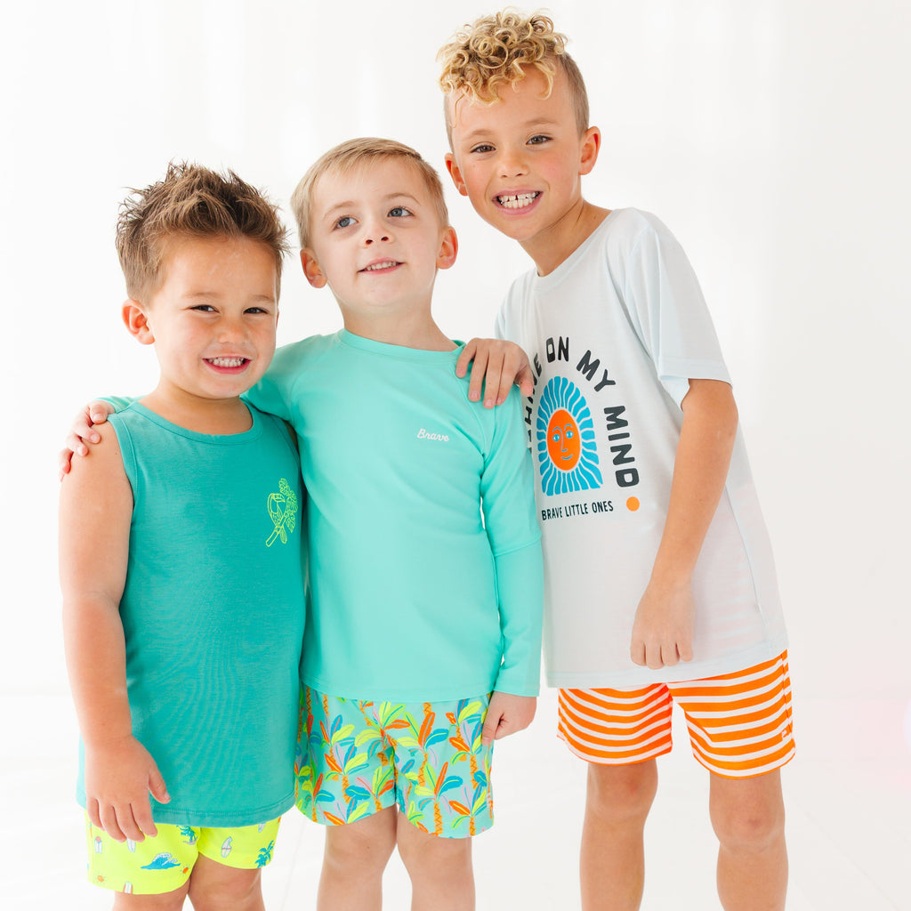 Three children wearing colorful brave little ones swimwear standing together on a white background