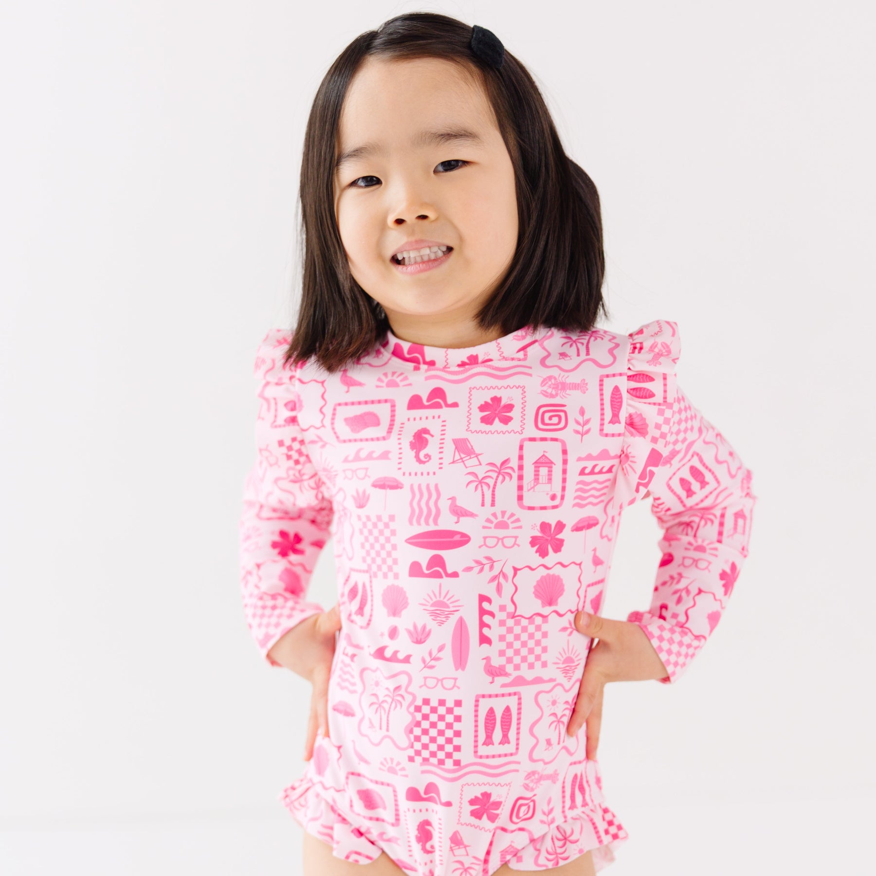 Child wearing a pink and white patterned long sleeve one-piece swimsuit on a white background