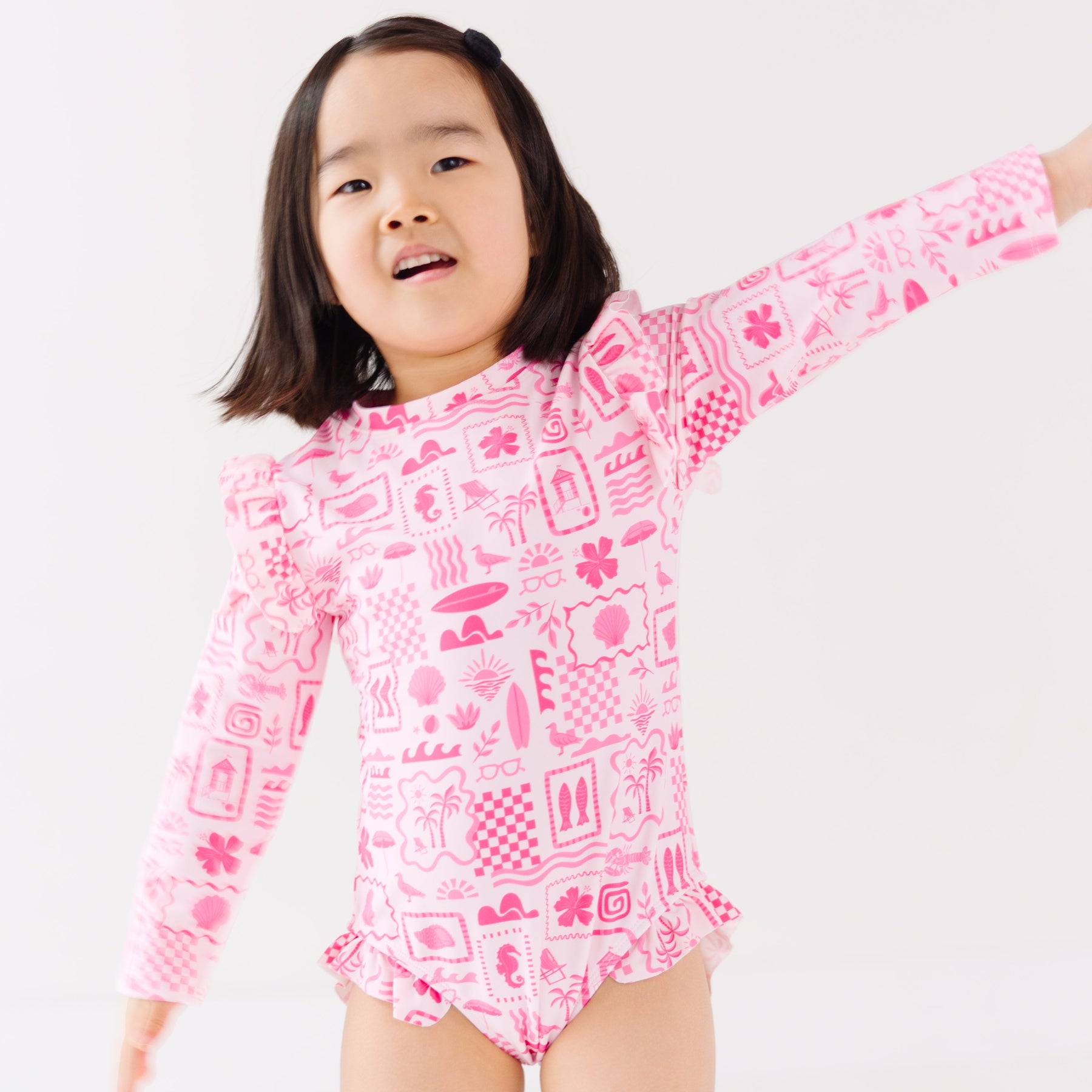 Child wearing a pink and white patterned long sleeve one-piece swimsuit on a white background