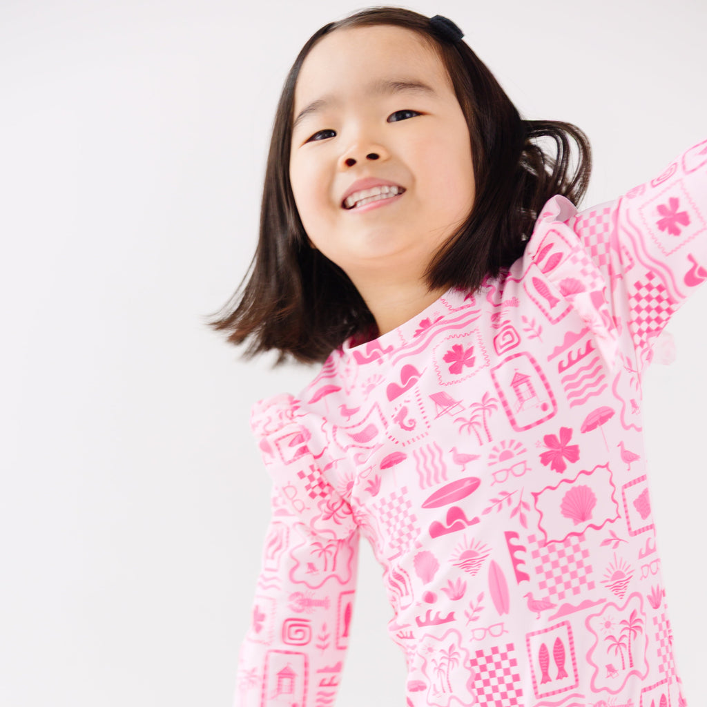 Child wearing a pink and white patterned long sleeve one-piece swimsuit on a white background