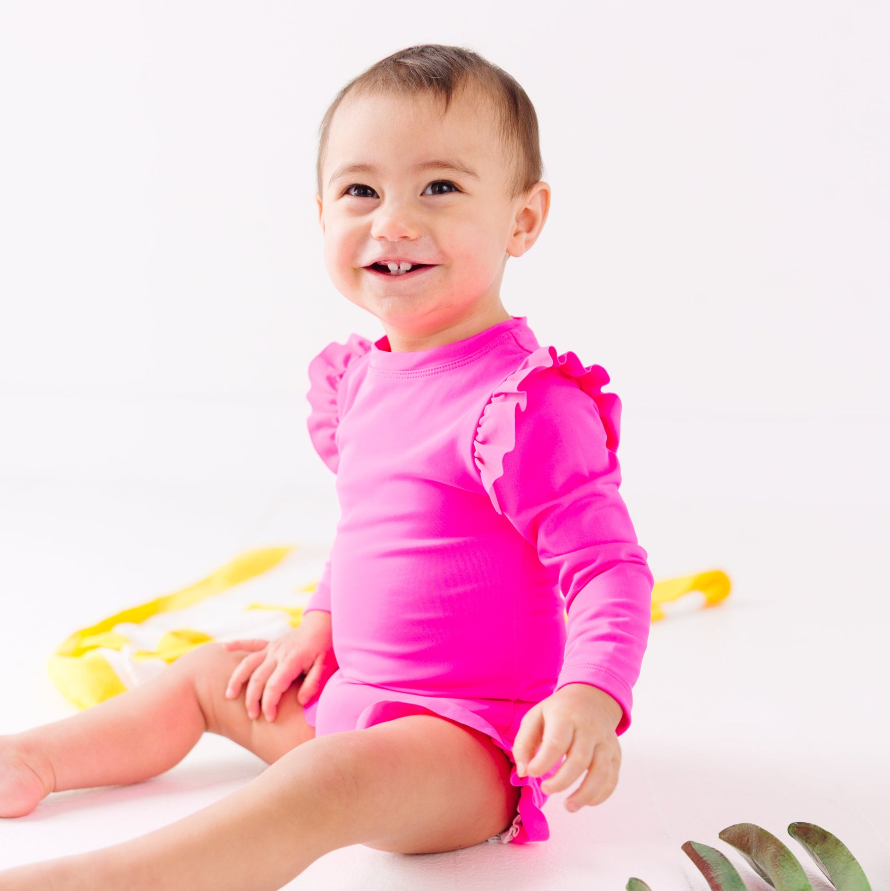 Baby wearing a bright pink one-piece swimsuit sitting on a white background.