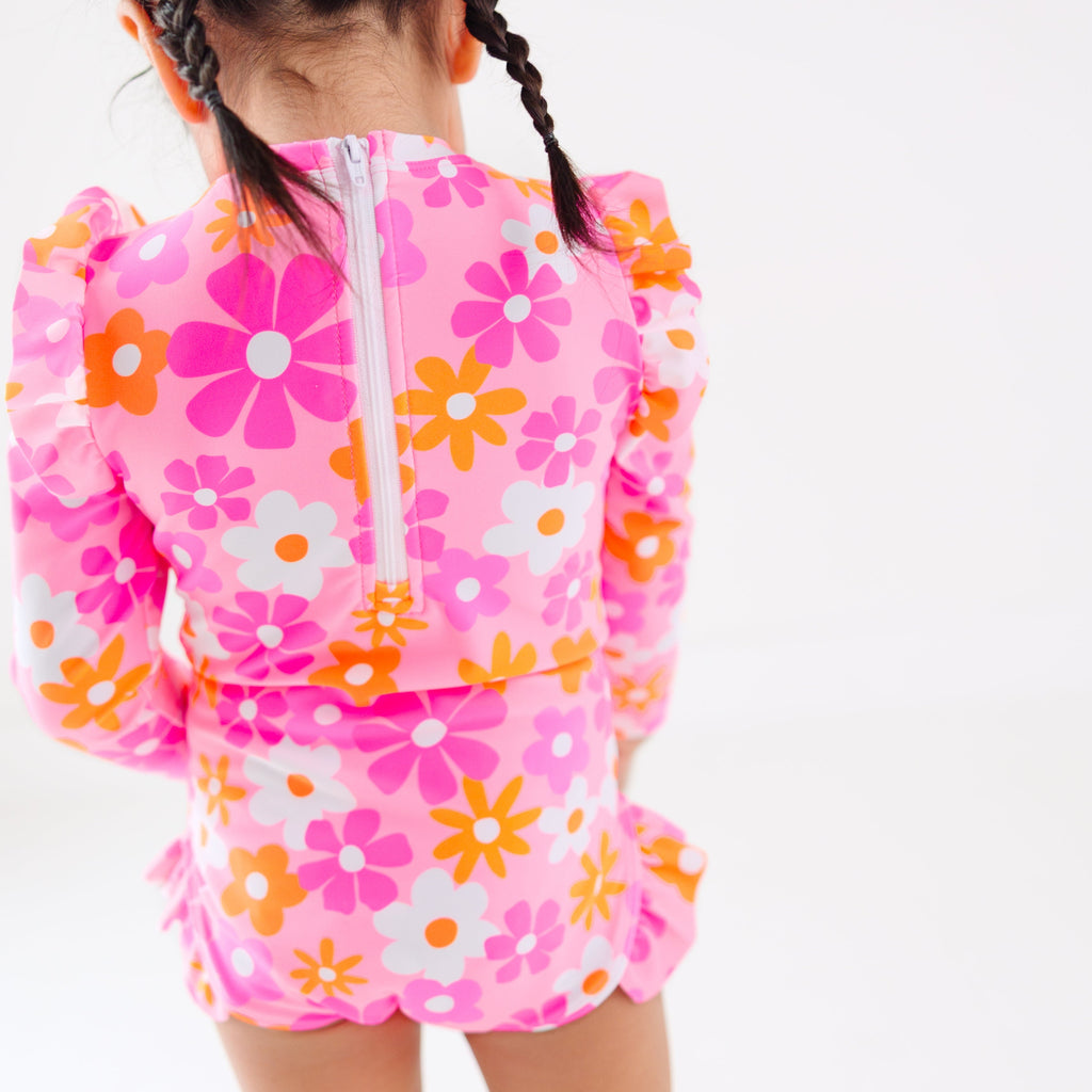 Back view of a child wearing a pink floral one-piece swimsuit on a white background