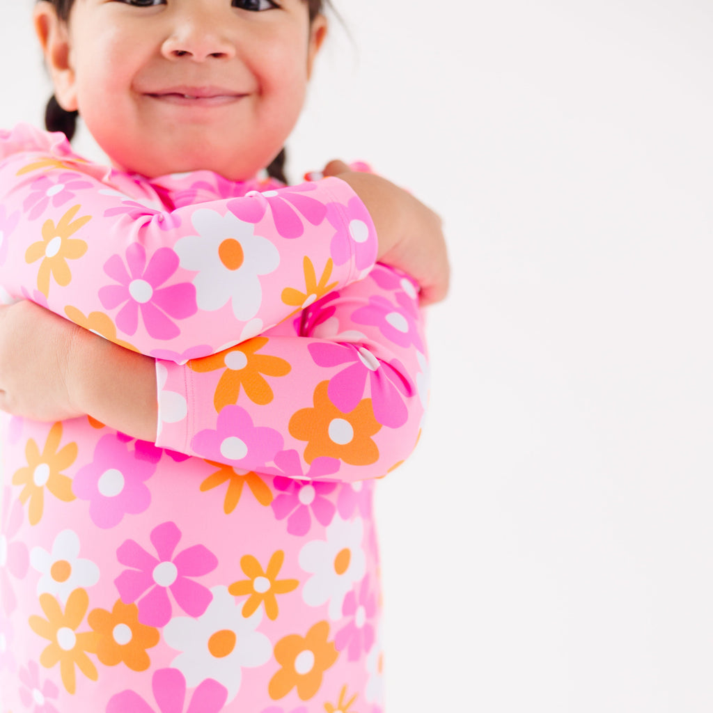 Close up shot of a child wearing a pink floral one-piece swimsuit on a white background