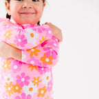 Close up shot of a child wearing a pink floral one-piece swimsuit on a white background