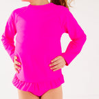 Close up view of a child wearing a bright pink long sleeve two-piece swimsuit on a white background