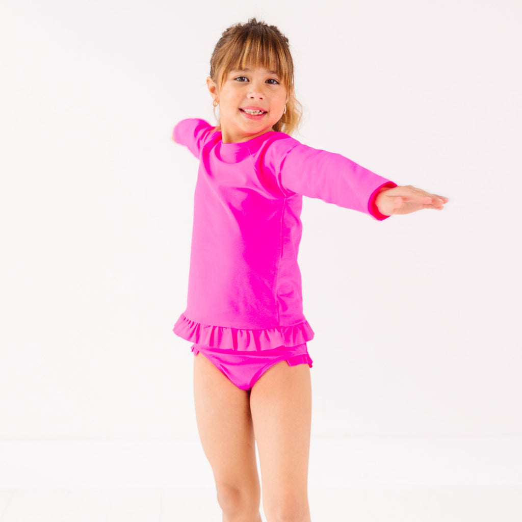 Child wearing a bright pink long sleeve two-piece swimsuit on a white background