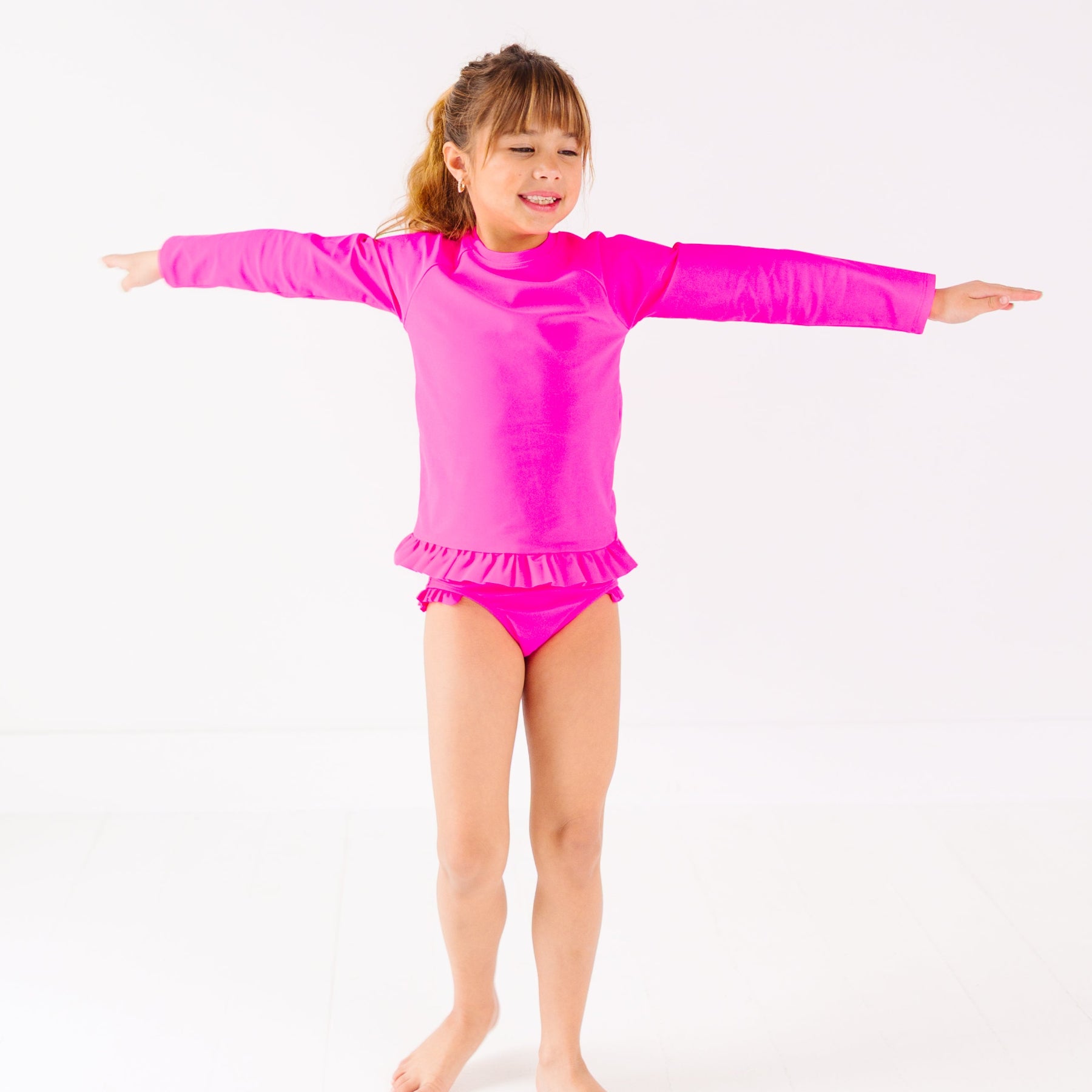Child wearing a bright pink long sleeve two-piece swimsuit on a white background