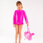 Child wearing a bright pink long sleeve two-piece swimsuit holding a matching pink hat on a white background