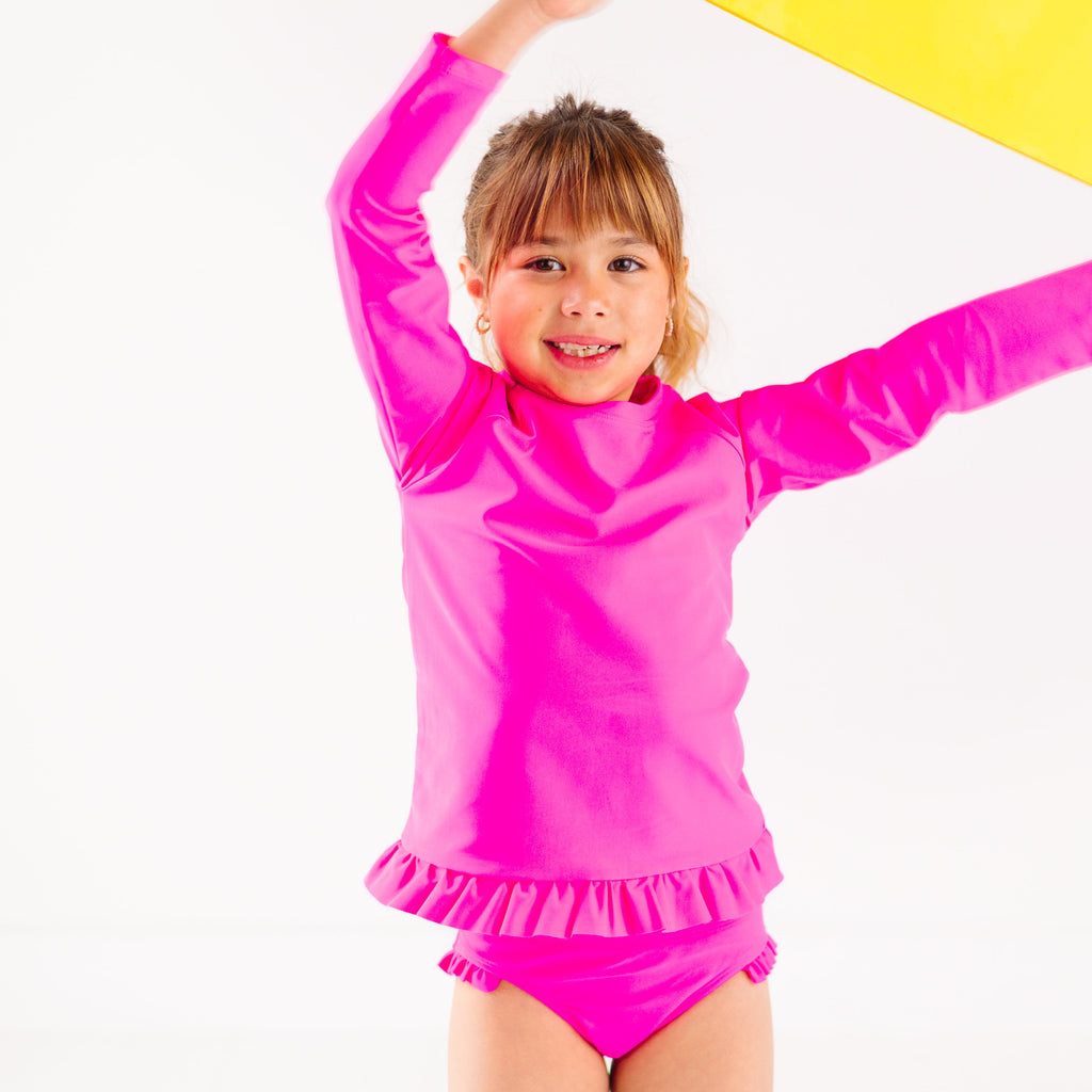 Child wearing a bright pink long sleeve two-piece swimsuit, holding a part of a yellow sun-shaped object