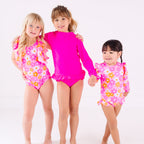 Three children wearing pink swimsuits with floral patterns on a white background