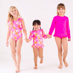 Three children wearing pink swimsuits with floral patterns on a white background
