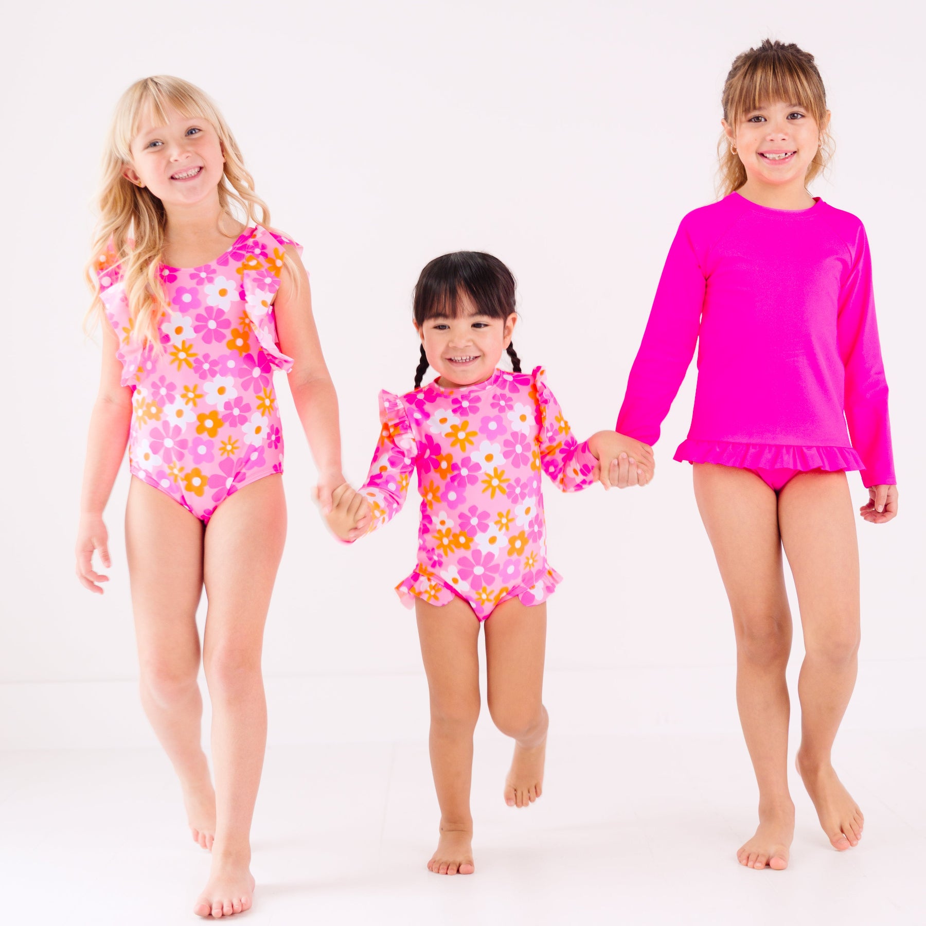 Three children wearing pink swimsuits with floral patterns on a white background