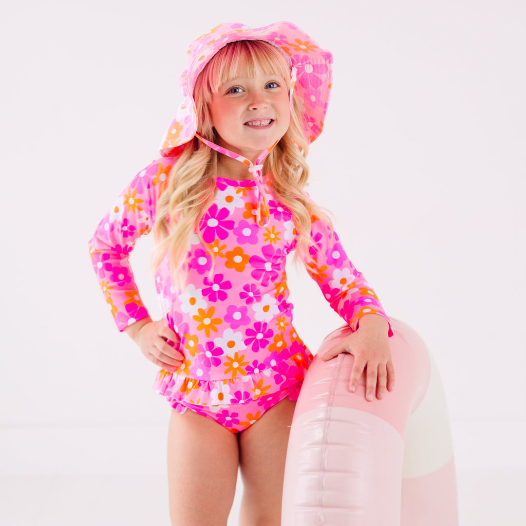 Child wearing a pink floral two-piece swimsuit and a matching sun hat while holding a pink floatie