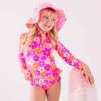 Child wearing a pink floral two-piece swimsuit and a matching sun hat while holding a pink floatie