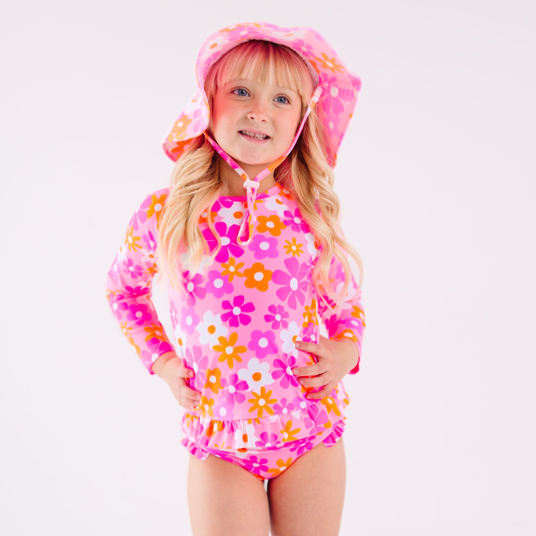 Child wearing a pink floral two-piece swimsuit and a matching sun hat on a white background