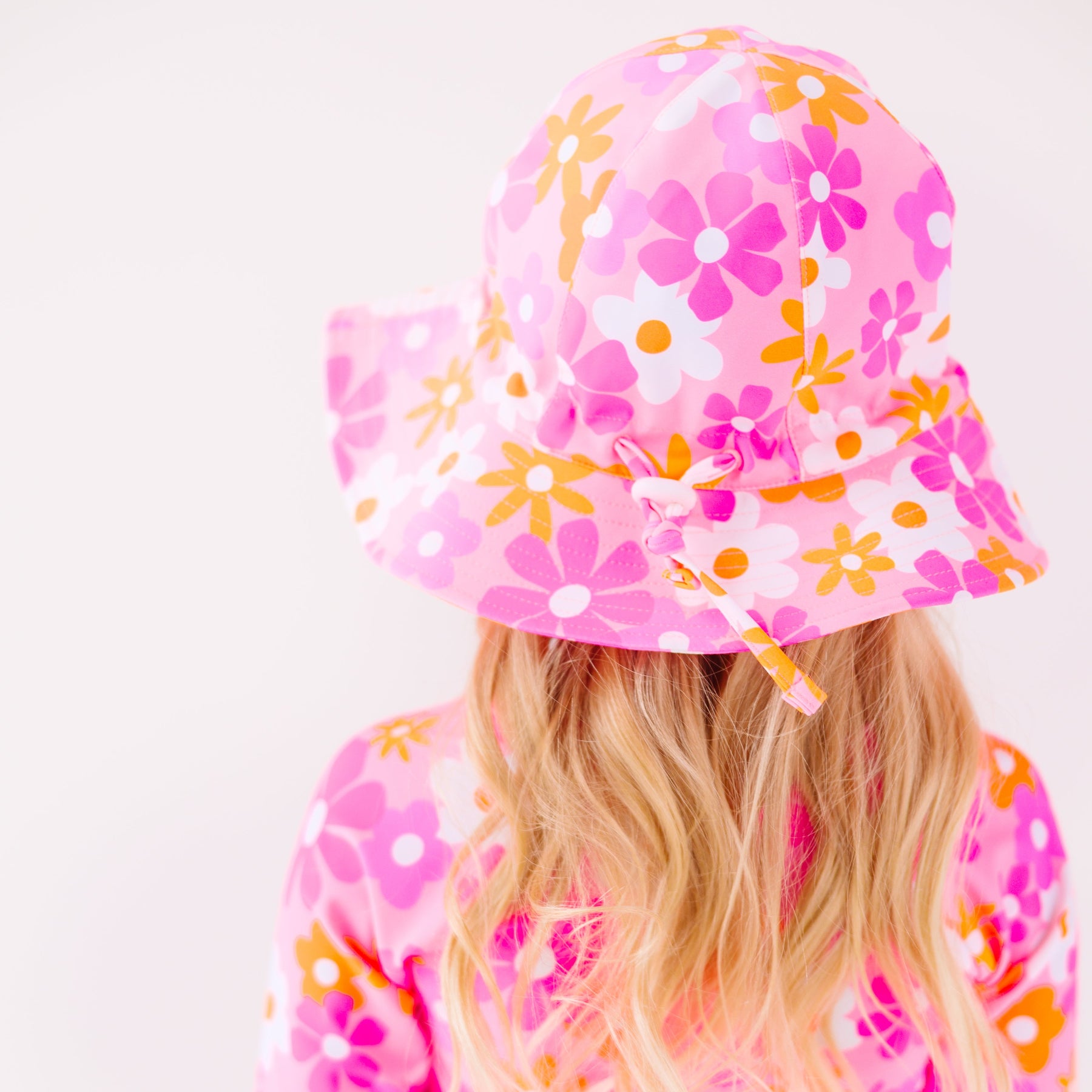 Back view of a child wearing a floral patterned sun hat and matching swimsuit