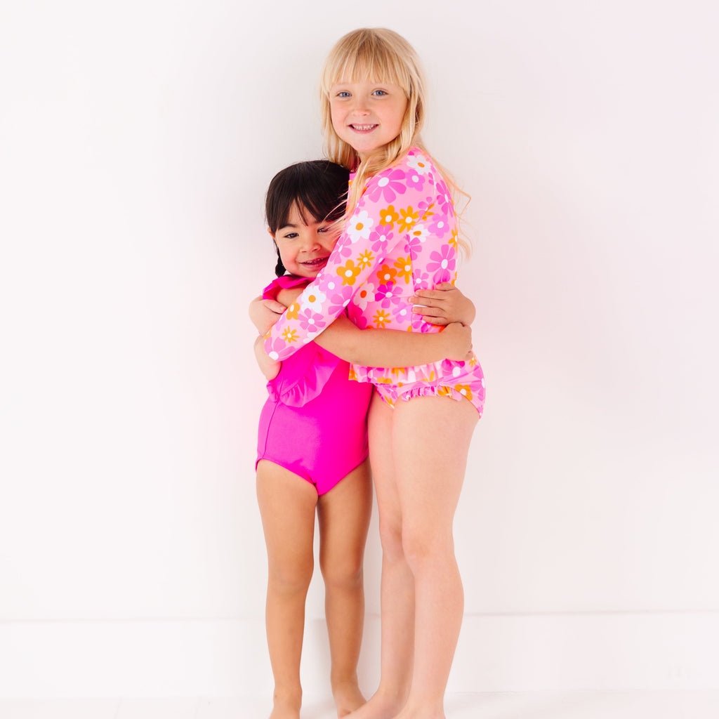 Two children in matching pink swimsuits standing on a white background