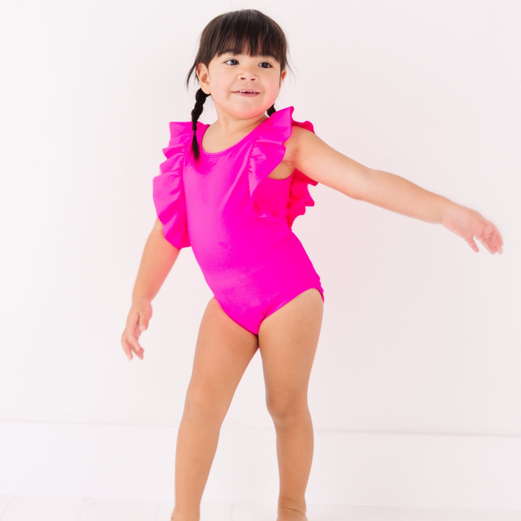 Young girl wearing a bright pink swimsuit with ruffled details on a white background