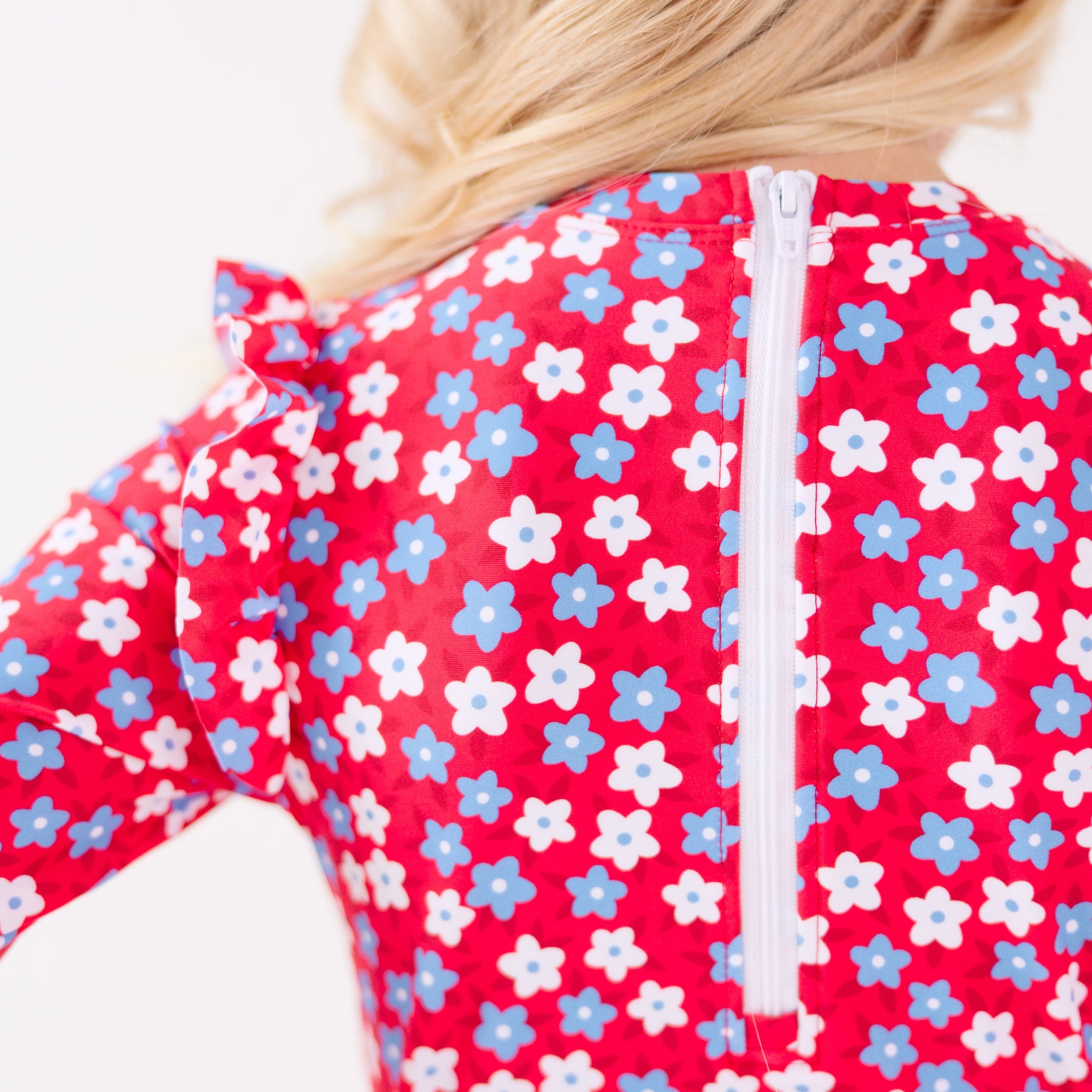 Close up of a young girl's back view wearing a red floral swimsuit on a white background
