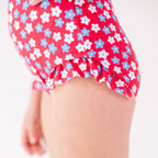 Close up of a young girl wearing a red floral swimsuit on a white background