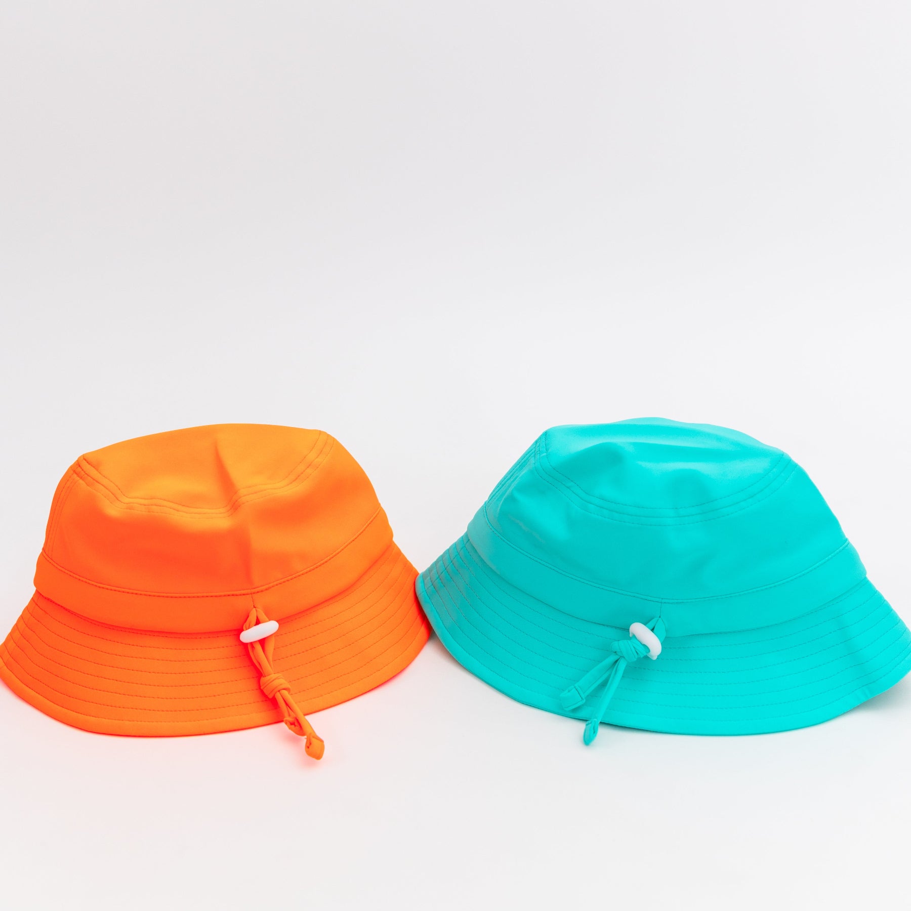 Two bucket hats, one orange and one teal, on a white background