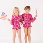 Two children in matching red and white swimsuits holding American flags on a white background