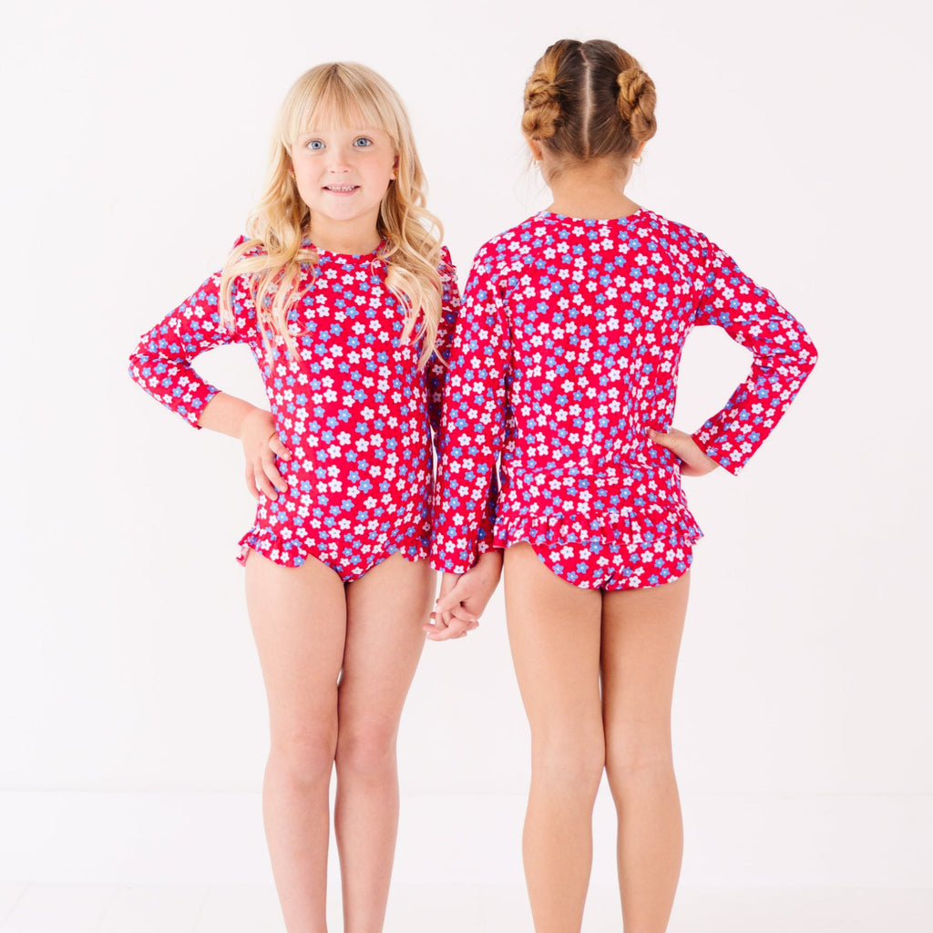 Two children wearing matching red and white floral patterned swimsuits on a white background