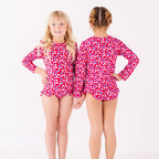 Two children wearing matching red and white floral patterned swimsuits on a white background