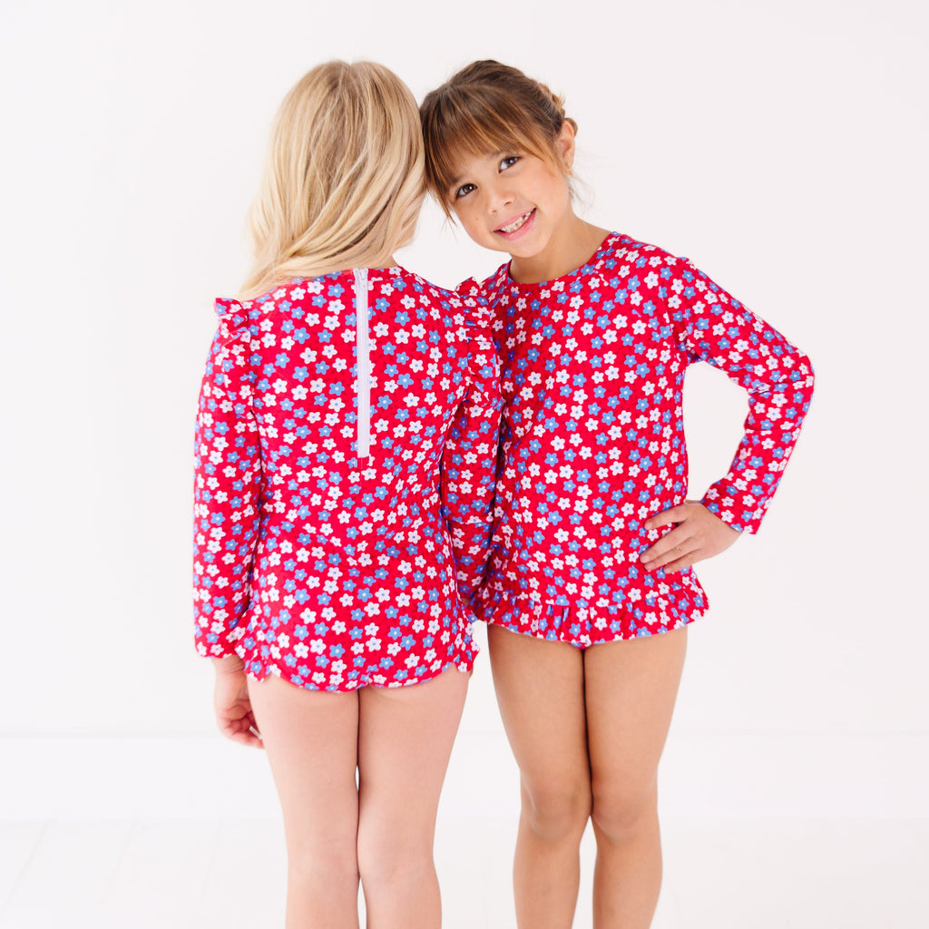 Two children wearing matching red and white floral patterned swimsuits on a white background