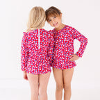 Two children wearing matching red and white floral patterned swimsuits on a white background
