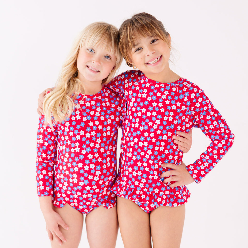 Two children wearing matching red and white floral patterned swimsuits on a white background