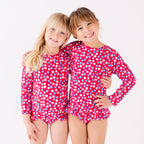 Two children wearing matching red and white floral patterned swimsuits on a white background