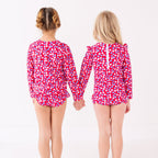 Two children wearing matching red and white floral patterned swimsuits on a white background